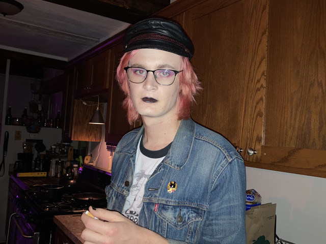 Quinn Decker holding a cigarette and looking at the camera in a kitchen